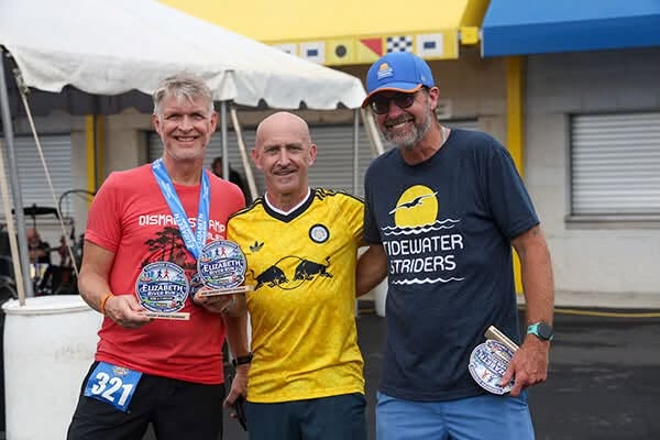 Three runners at the Elizabeth River Run 10K awards ceremony; runner in the middle wears a yellow football shirt