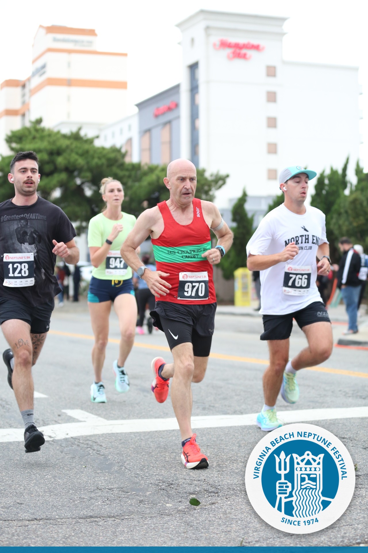 Runner wearing red and green Les Croupiers Cardiff vest and bib 970 racing at the Neptune Festival 8K